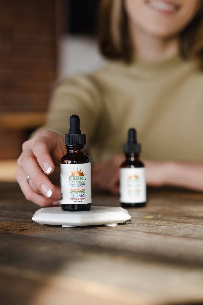 Close-up of a hand reaching for CBD oil bottle with dropper on wooden table.
